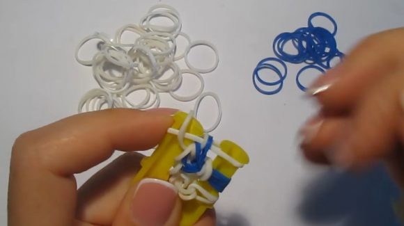 Плетение браслета из синих и белых резинок на жёлтой рогатке