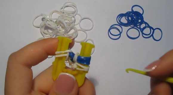 Плетение браслета из белых и синих резинок на жёлтой рогатке